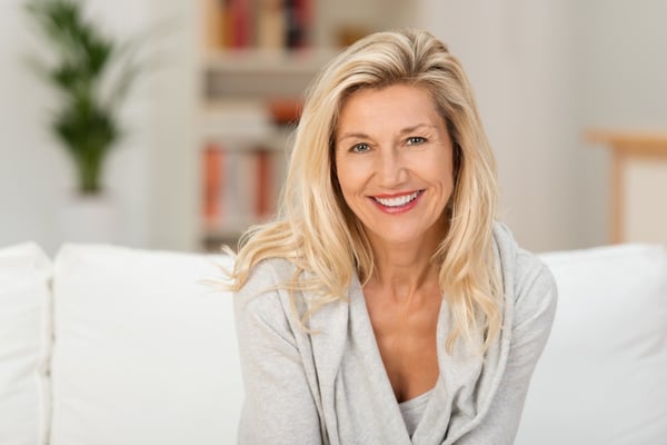 Lovely middle-aged blond woman with a beaming smile sitting on a sofa at home looking at the camera.jpeg